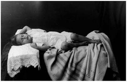 Fotografía de niña muerta posando “como dormida” realizada por el fotógrafo colombiano Luis Melitón Rodríguez Márquez (1875-1942), en 1908. Manejando la toma con gran habilidad estética, el fotógrafo invita al espectador a mantenerse en un respetuoso silencio (Osorio Cossio, 2016).